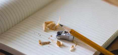 A pencil is balanced on an open lined notebook with a sharpener and sharpenings.