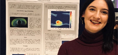 A photograph of Rebecca Humble standing in front of her research poster
